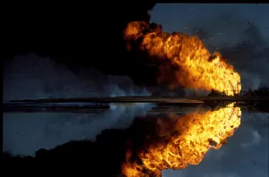 Oil well fire with flames reflected in floodwater, link to Kuwait 1991 fire images gallery